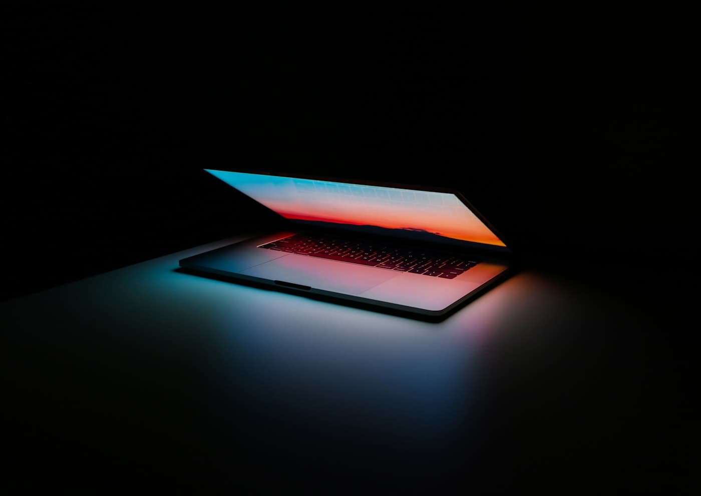 MacBook with colorful screen glow on dark background